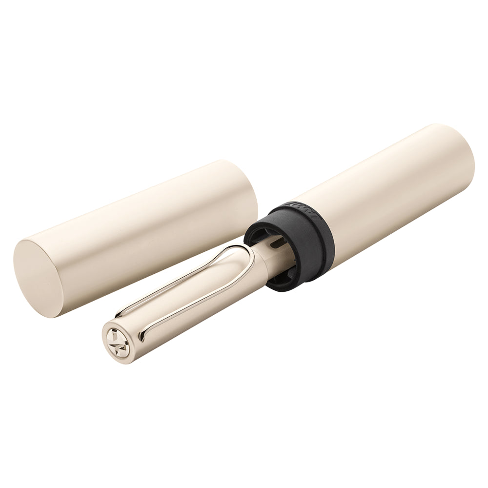 Un écrin ouvert contenant le stylo plume Lamy Crème LX Palladium est posé sur un fond blanc. L'écrin présente un design simple sous forme cylindrique et élégant, mettant en valeur le stylo avec une finition palladium et crème, avec le logo de la marque visible.