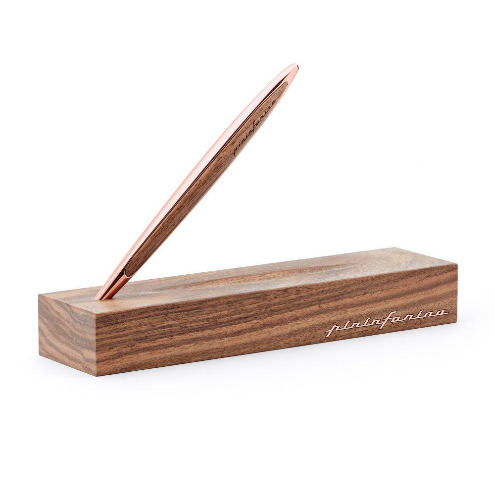 Stylo Forever Pininfarina Cambiano en or rose posé sur son emplacement, celui-ci lui permet de tenir à 45° sur sa base assortie qui sert aussi d'écrin, présentée sur un fond blanc. L'écrin met en valeur la finition luxueuse du stylo et souligne son design moderne et innovant, parfait pour ceux qui recherchent une écriture élégante et durable.
