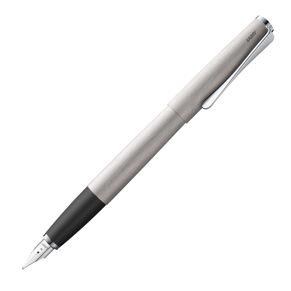 Un stylo plume Lamy Studio en finition brossée 065, incliné à 45 degrés avec le bouchon retiré, est présenté sur un fond blanc. Le stylo plume se caractérise par sa finition en métal brossé, offrant un design moderne et raffiné, typique de la collection Studio.