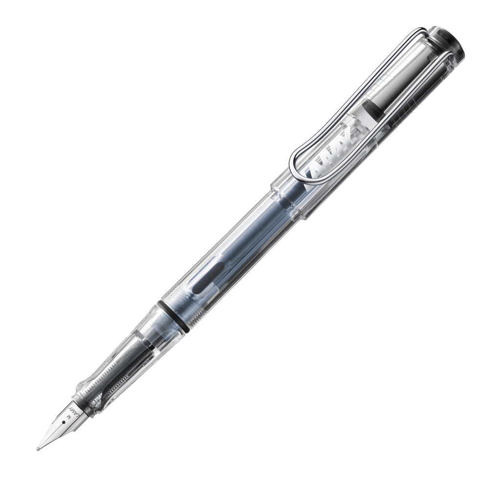 Un stylo plume Lamy Vista transparent, incliné à 45 degrés avec le bouchon retiré, est présenté sur un fond blanc. Ce stylo plume se distingue par son corps en plastique transparent, permettant de voir l'encre à l'intérieur et la plume de taille M, offrant un design moderne et fonctionnel.